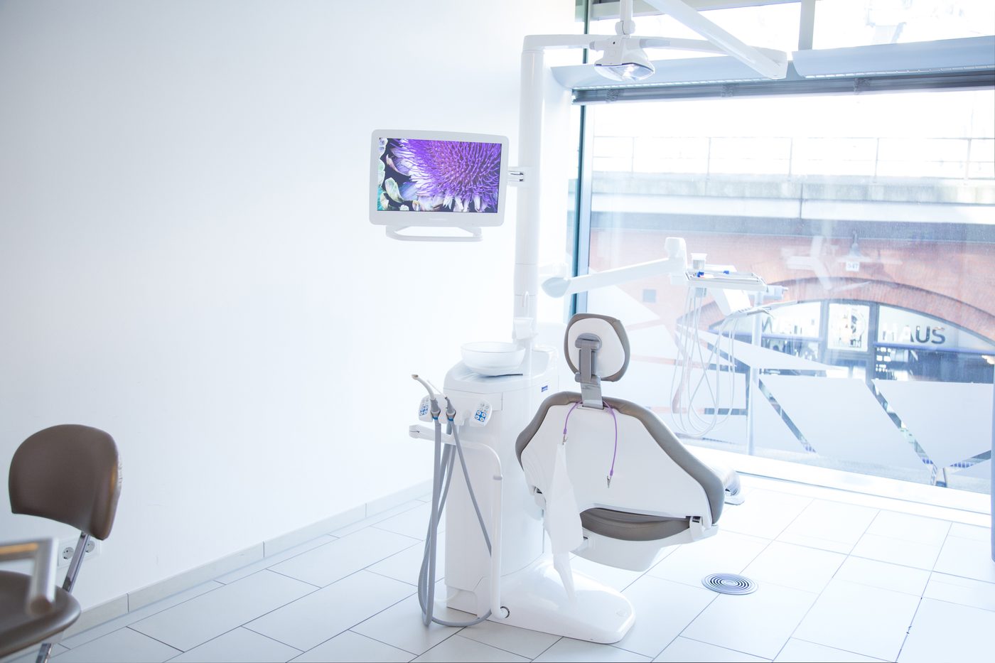 Behandlungszimmer mit Behandlungsstuhl, Monitor und großem Fenster
