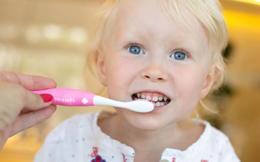 Kleinkind bekommt die Zähne mit einer rosa Kinderzahnbürste geputzt